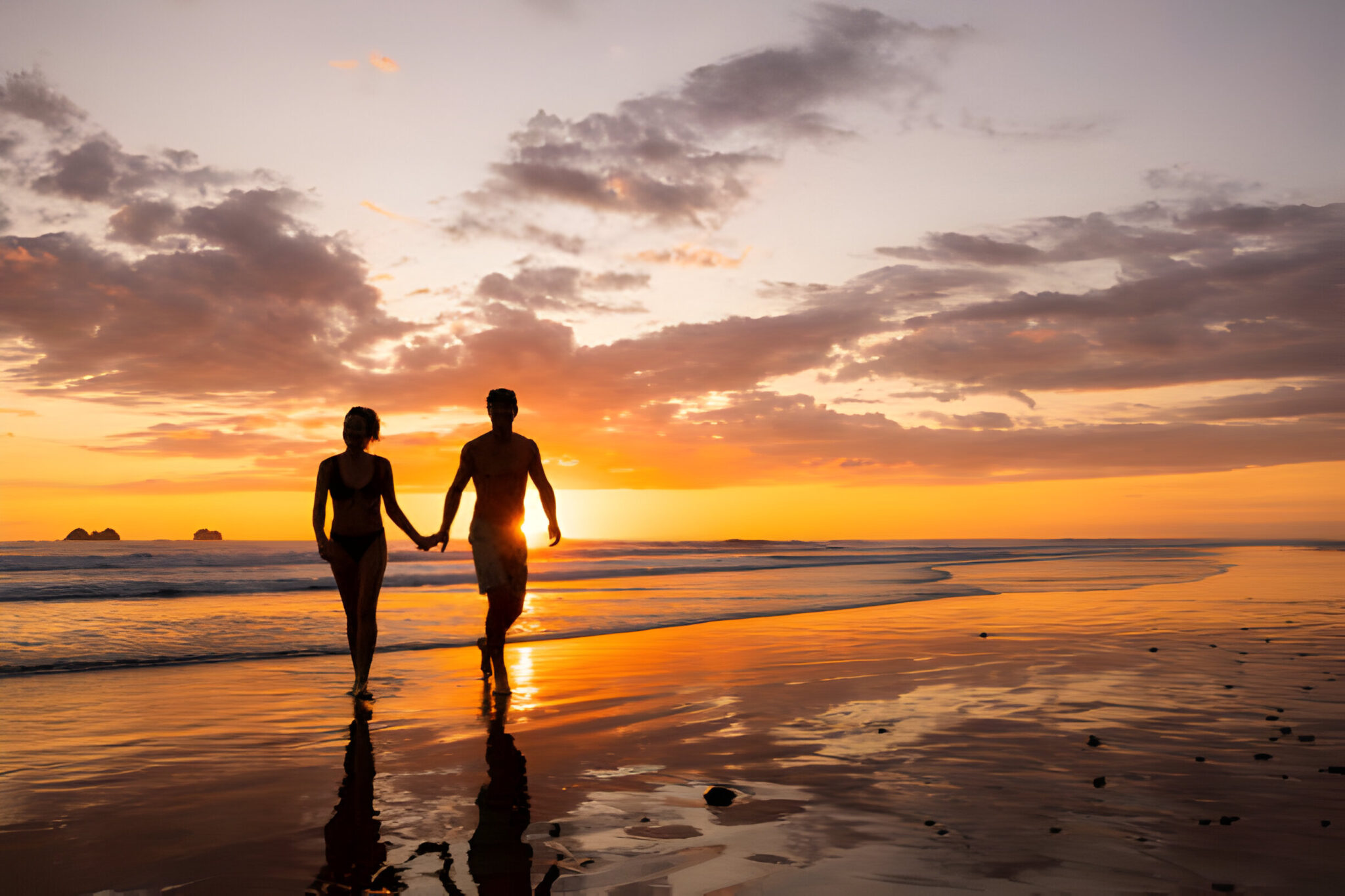 A couple walking out of the ocean at sunset